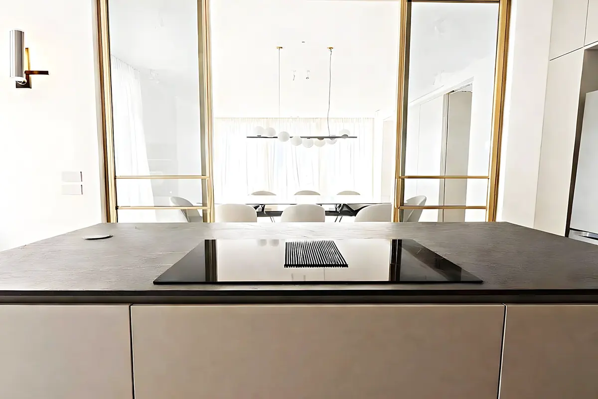 Isla con placa de inducción y extracción integrada, y carpintería de latón al fondo