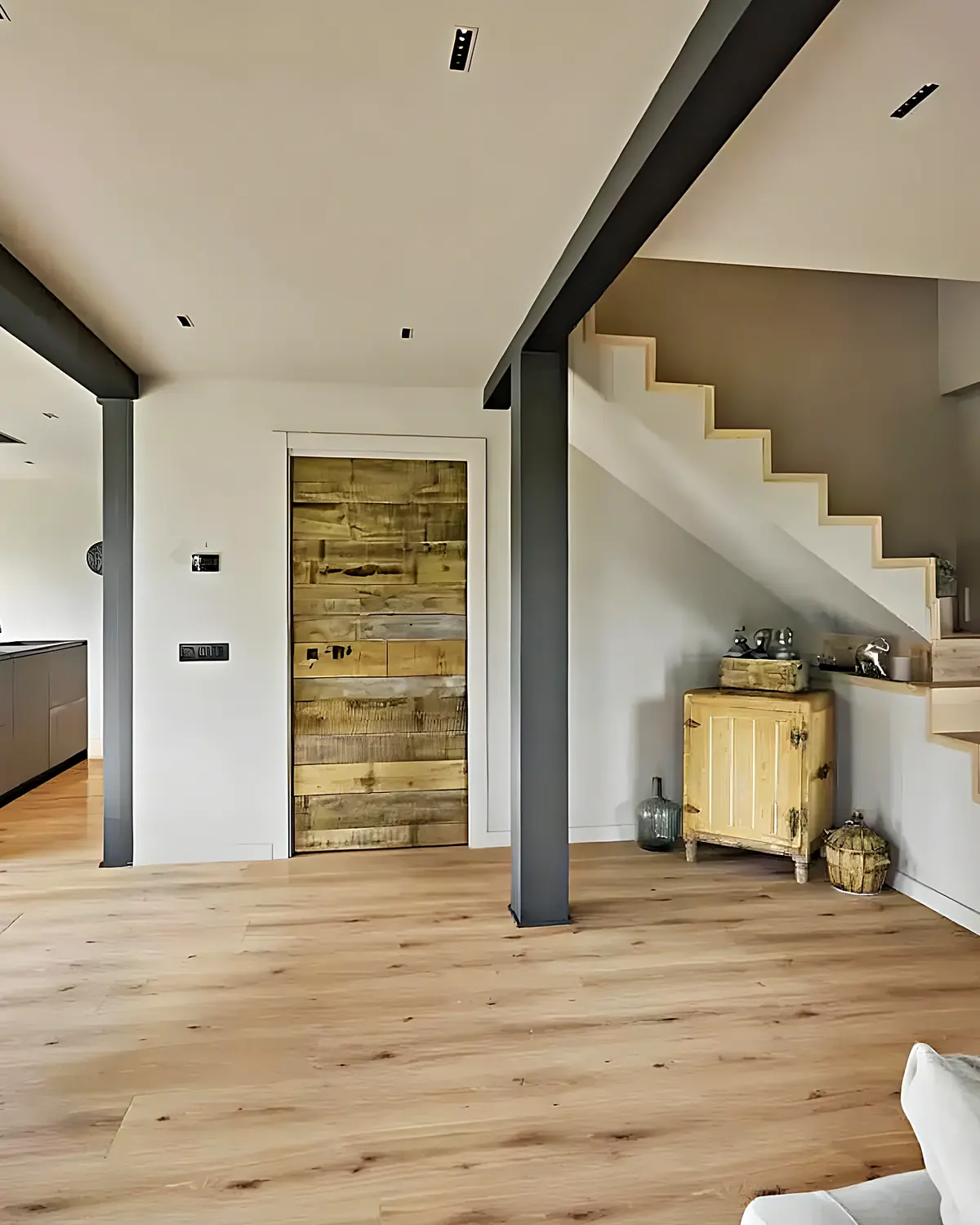 Salón diáfano con el pilar de acero negro visto y la escalera de obra al fondo